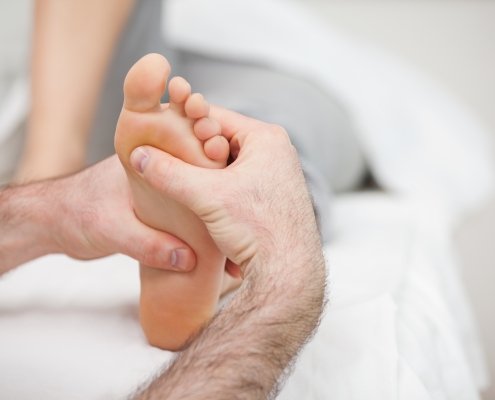 Man using his two hands to massage a foot in a room